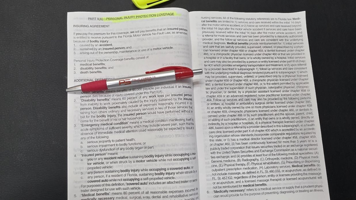 A Progressive auto policy booklet open to the Personal Injury Protection coverage page, with a Phillip Stamman, P.A. pen resting across it